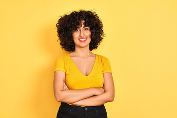 Young arab woman with curly hair wearing t-shirt standing over isolated yellow background happy face smiling with crossed arms looking at the camera. Positive person.