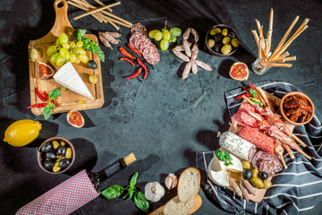 Antipasto platter with ham, prosciutto, salami, blue cheese, mozzarella, olives, grissini bread sticks with pesto and red wine on a dark background