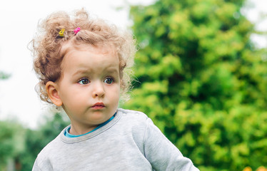 portrait of a little cute beautiful girl in surprise looks into the distance and into the camera. cute baby outdoors. happy childhood.