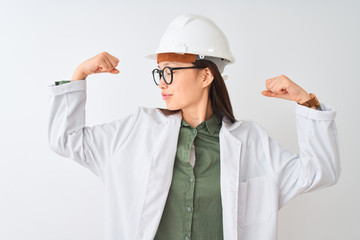 Young chinese engineer woman wearing coat helmet glasses over isolated white background showing arms muscles smiling proud. Fitness concept.