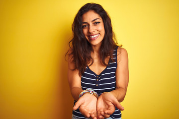 Young beautiful woman wearing striped t-shirt standing over isolated yellow background Smiling with hands palms together receiving or giving gesture. Hold and protection