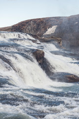 A three-step staircase of the Gullfoss waterfall on Hvita river, as pictured in detail (water plunging into the canyon, mossy cliffs, thick spray, panorama of the rapids)