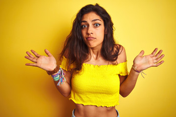 Young beautiful woman wearing casual t-shirt standing over isolated yellow background clueless and...