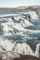 A three-step staircase of the Gullfoss waterfall on Hvita river, as pictured in detail (water plunging into the canyon, mossy cliffs, thick spray, panorama of the rapids)