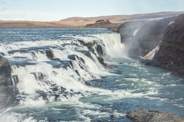 A three-step staircase of the Gullfoss waterfall on Hvita river, as pictured in detail (water plunging into the canyon, mossy cliffs, thick spray, panorama of the rapids)