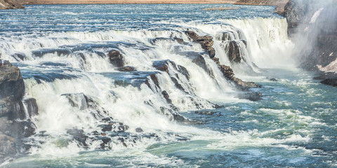 A three-step staircase of the Gullfoss waterfall on Hvita river, as pictured in detail (water plunging into the canyon, mossy cliffs, thick spray, panorama of the rapids)
