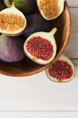 Ripe fresh fig fruits lie in a wooden bowl on a light wood background. Whole figs and slices. Close-up. View from above.