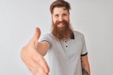 Young redhead irish man wearing grey polo standing over isolated white background smiling friendly offering handshake as greeting and welcoming. Successful business.