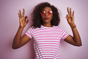 Young african american woman wearing t-shirt and sunglasses over isolated pink background relax and smiling with eyes closed doing meditation gesture with fingers. Yoga concept.