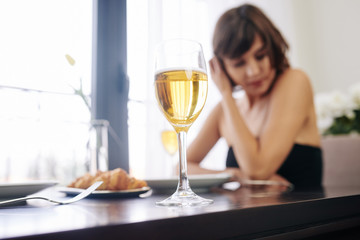 Glass of white wine of young woman sitting at restaurant table alone and waiting for her date