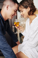 Smiling boyfriend and girlfriend touching foreheads and looking at glass of wine