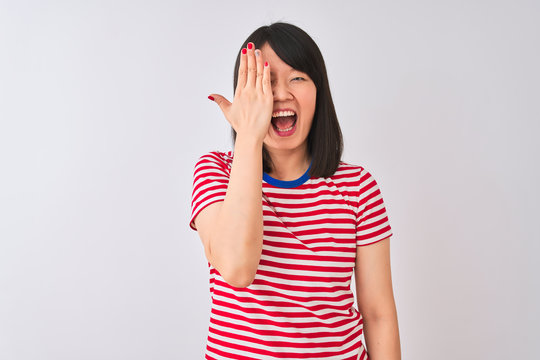 Young beautiful chinese woman wearing red striped t-shirt over isolated white background covering one eye with hand, confident smile on face and surprise emotion.