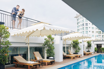 Young flirting couple standing at hotel balcony and drinking juice or fruit cocktail