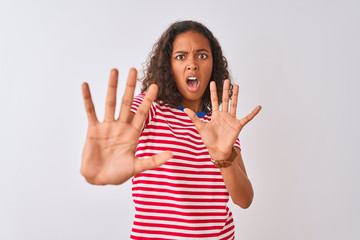 Young brazilian woman wearing red striped t-shirt standing over isolated white background afraid and terrified with fear expression stop gesture with hands, shouting in shock. Panic concept.