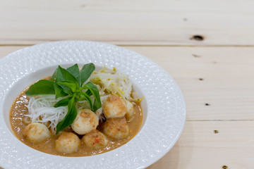 Thai Food. Rice Noodles in Fish Curry With fish balls, pork snack, basil, bean sprouts on top, placed on a wooden table.