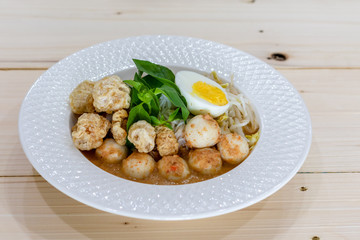 Asian Food Rice Noodles in Fish Curry With boiled egg, fish balls, pork snack, basil, bean sprouts on top, placed on a wooden table.
