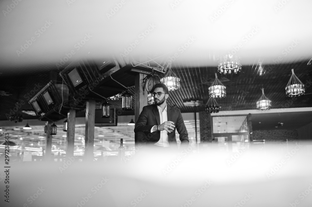 Wall mural Handsome well-dressed arabian man with glass of whiskey and cigar posed at pub.