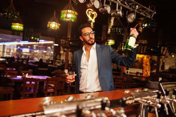 Handsome well-dressed arabian man with glass of whiskey and cigar posed at pub.