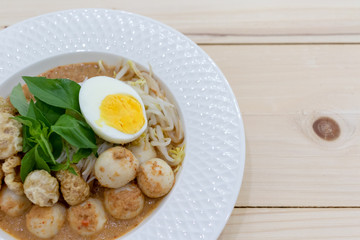 Asian Food. Rice Noodles in Fish Curry With boiled egg, fish balls, pork snack, basil, bean sprouts on top, placed on a wooden table.
