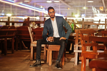 Handsome well-dressed arabian man with glass of whiskey and cigar posed at pub.