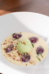 Close up of ice cream dessert with a scoop of pistachio ice cream, plums, almonds and creamy sauce as a fine dining meal