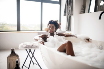 Curly dark-eyed woman lying and chilling in bath with foam