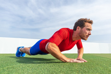 Fitness man doing diamond hand push ups exercises at outdoor grass park. Core body workout athlete planking or doing pushup.