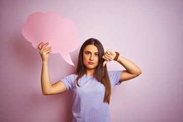 Young beautiful woman holding cloud speech bubble over isolated pink background with angry face, negative sign showing dislike with thumbs down, rejection concept