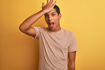 Young handsome arab man wearing striped t-shirt standing over isolated yellow background surprised with hand on head for mistake, remember error. Forgot, bad memory concept.