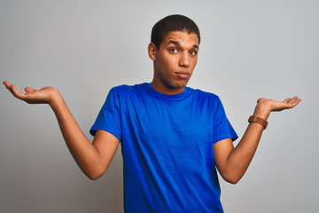 Young handsome arab man wearing blue t-shirt standing over isolated white background clueless and confused expression with arms and hands raised. Doubt concept.