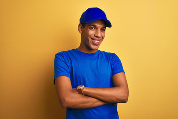 Young handsome arab delivery man standing over isolated yellow background happy face smiling with crossed arms looking at the camera. Positive person.