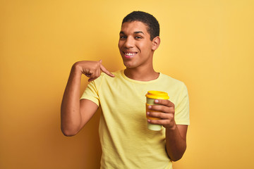 Young handsome arab man drinking take away coffee over isolated yellow background with surprise face pointing finger to himself