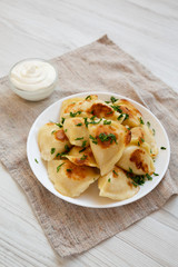 Homemade traditional polish fried potato pierogies on a white plate, side view.