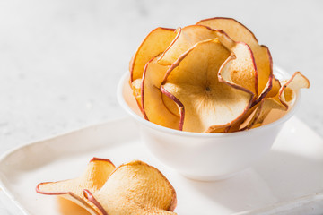 Apple chips in a white bowl on the table. Place for text	