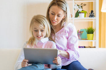 Blonde cheerful girl with her mother using tablet computer together