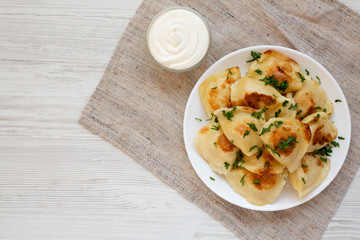 Homemade traditional polish fried potato pierohy on a white plate with sour cream, top view. Overhead, from above, flat lay. Copy space.