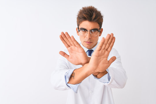 Young handsome sciencist man wearing glasses and coat over isolated white background Rejection expression crossing arms and palms doing negative sign, angry face