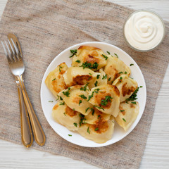 Homemade traditional polish fried potato pierogis on a white plate with sour cream, top view....