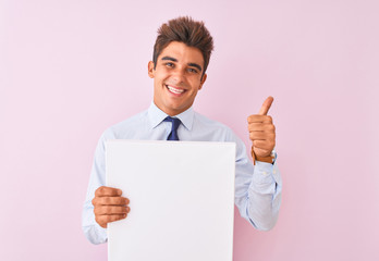 Young handsome businessman holding banner standing over isolated pink background happy with big smile doing ok sign, thumb up with fingers, excellent sign