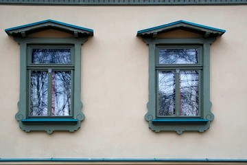 Fototapeta na wymiar Two windows in an old house in a city park. Beautiful platbands and reflection in glasses.