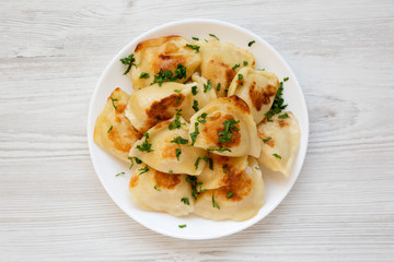 Homemade traditional polish fried potato pierogis on a white plate on a white wooden background,...