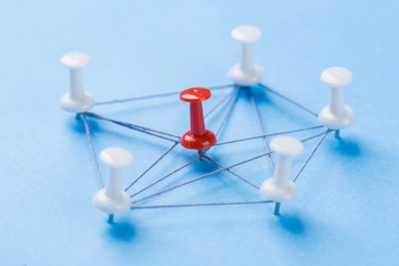 network with red and white pins and string, An arrangement of colorful pins linked together with string on a blue background suggesting a network of connections.