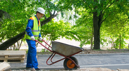 a worker in a white helmet and blue uniform carries a cart to a landfill to take out the trash