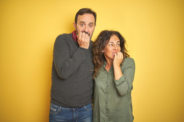 Fototapeta premium Beautiful middle age couple over isolated yellow background looking stressed and nervous with hands on mouth biting nails. Anxiety problem.