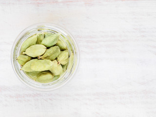 Spice grains Green Cardamom (Elettaria cardamomum) in a glass jar on a white wooden background