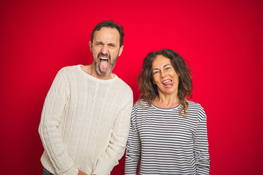Beautiful middle age couple wearing winter sweater over isolated red background sticking tongue out happy with funny expression. Emotion concept.