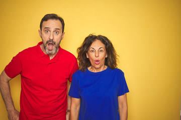 Fototapeta premium Beautiful middle age couple together standing over isolated yellow background afraid and shocked with surprise expression, fear and excited face.