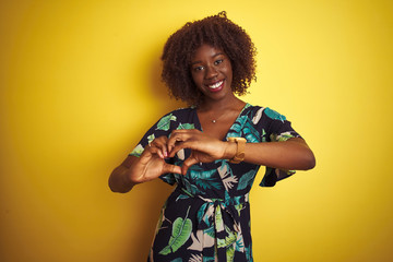 Young african afro woman wearing summer floral dress over isolated yellow background smiling in love showing heart symbol and shape with hands. Romantic concept.