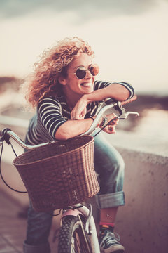 Cheerful trendy young adult caucasian woman sitting on a bike and smiling - beautiful female portrait - concept of outdoor leisure activity and happiness and joyful lifestyle