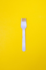 One wooden fork on saturated yellow background as a symbol of consumption. Eco and fast food concept.